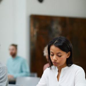 Portrait of mixed-race businesswoman writing notes while sitting at table in class during six sigma lecture, copy space